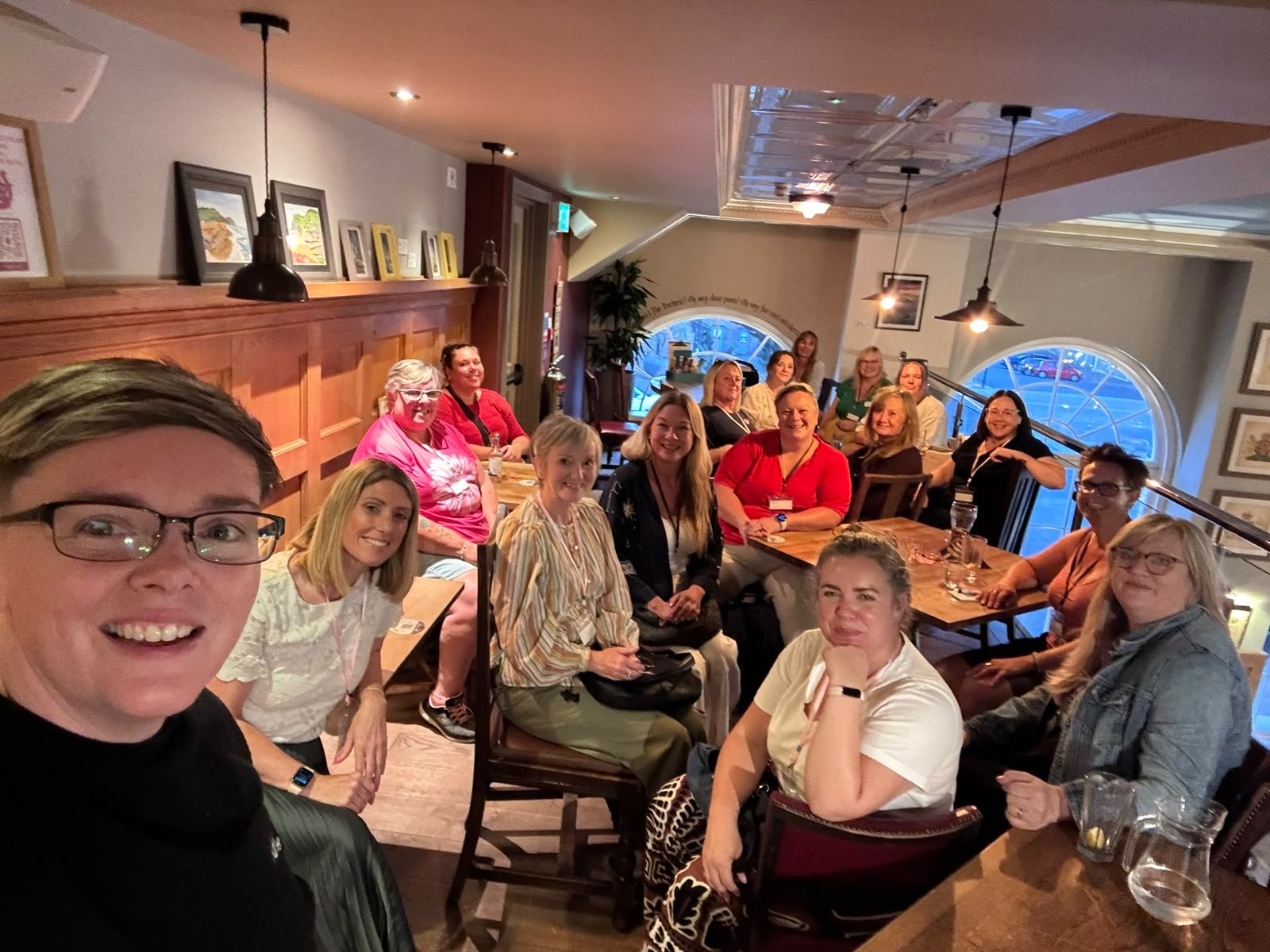 A table full of HerHustle women smiling at the camera in a group selfie at a pub meet-up.